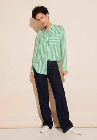 Green and white striped button-up shirt with a chest pocket, paired with dark blue wide-leg jeans and white sneakers. Simple design, casual fit.