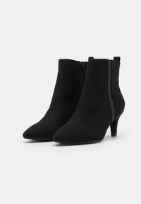 Botas de tobillo de ante negro con punta afilada, cierre de cremallera y detalles de malla decorativa en los laterales. Cuentan con un tacón delgado.