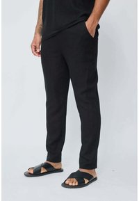 Pantalons noirs fuselés en tissu léger avec poches, associés à des sandales noires à semelle plate avec un design à brides croisées.