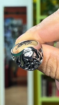 Srebrn prstan z izklesanim motivom lobanje, ki ima podrobne detajle. Gladek notranji del obroča in sijoč zaključek. Vidni prst, ki drži prstan.