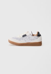 Zapatilla baja con tela de lentejuelas blanca, detalles de ante beige, suela de goma, cordones blancos y un tirador negro en el talón con costuras blancas.