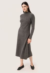 Abito a maglia grigio a maniche lunghe con collo alto, caratterizzato da una vestibilità comoda e una silhouette fluida, indossato con scarpe nere basse.