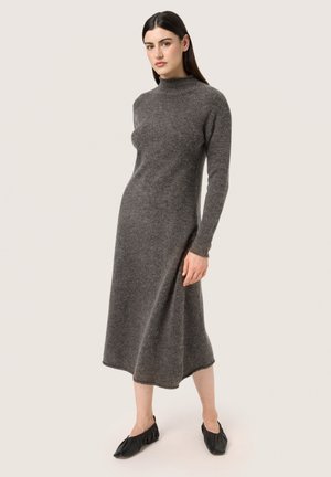 Abito a maglia grigio a maniche lunghe con collo alto, caratterizzato da una vestibilità comoda e una silhouette fluida, indossato con scarpe nere basse.