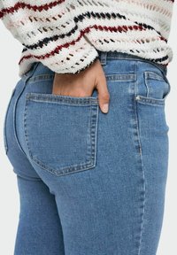 Mėlynos džinsinės kelnės su prigludusia siluetu. Su užpakaline kišene ir subtiliu blukimu. Derinamos su daugiaspalviu raštuotu megztiniu.