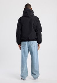 Schwarze Kapuzenjacke mit lockerer Passform, kontrastierenden gerippten Bündchen und Saum, kombiniert mit lockeren, hellblauen Jeans.