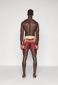 Bañador de satén en rojo intenso con una cinturilla texturizada en beige. El diseño presenta un corte holgado y un acabado suave.