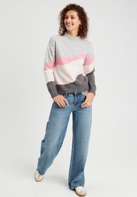 Grå sweater med lyserøde og hvide bølgemønstre, ribbet hals, parret med lyseblå wide-leg jeans og hvide sneakers. Casual outfit.