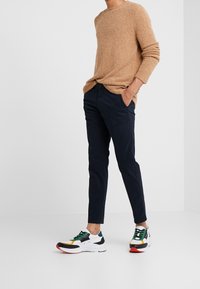 Maglione beige lavorato a maglia, pantaloni chino blu navy e scarpe da ginnastica multicolori con base bianca e suola rossa. Tessuto strutturato con vestibilità comoda.