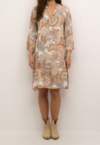 Sukienka w wzór paisley w kremowym, pomarańczowym i niebieskim kolorze, z półguzikowym zapięciem i rękawami o długości 3/4, zestawiona z tanowymi botkami sięgającymi kostki.