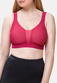 Różowy sportowy biustonosz w wzory z szerokimi ramiączkami, przezroczystym wzorem z siateczki oraz logo na pasku. Czarne legginsy o gładkiej fakturze z przeszyciami.