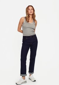 Top sin mangas gris combinado con jeans de tiro alto azul oscuro, con puños enrollados, y zapatillas deportivas blancas con detalles negros.