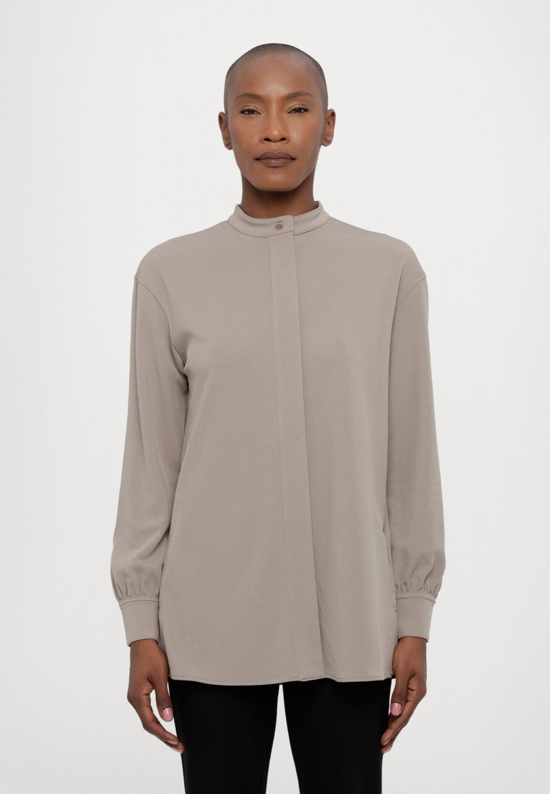 Beige bluse med lange ermer og høy krage, frontlukking med knapper og samlede mansjetter; glatt stoff med løs passform.