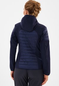 Marineblå hættejakke med quiltet tekstur på skulder- og rygpaneler. Glatte ærmer og yoke, der giver en kontrast i stof og design.