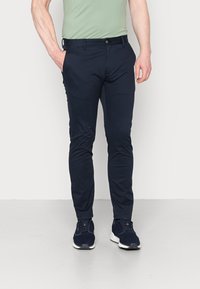 Chinos bleu marine ajustés en tissu lisse, avec un bouton frontale unique, des poches latérales et un design à longueur de cheville, associés à des baskets sombres.