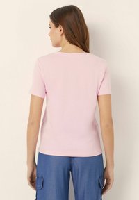 Světle růžová košile s krátkým rukávem a kulatým výstřihem, vyrobená z měkké látky, má rovný střih a jednoduchý design. Nosit s modrými kalhotami.
