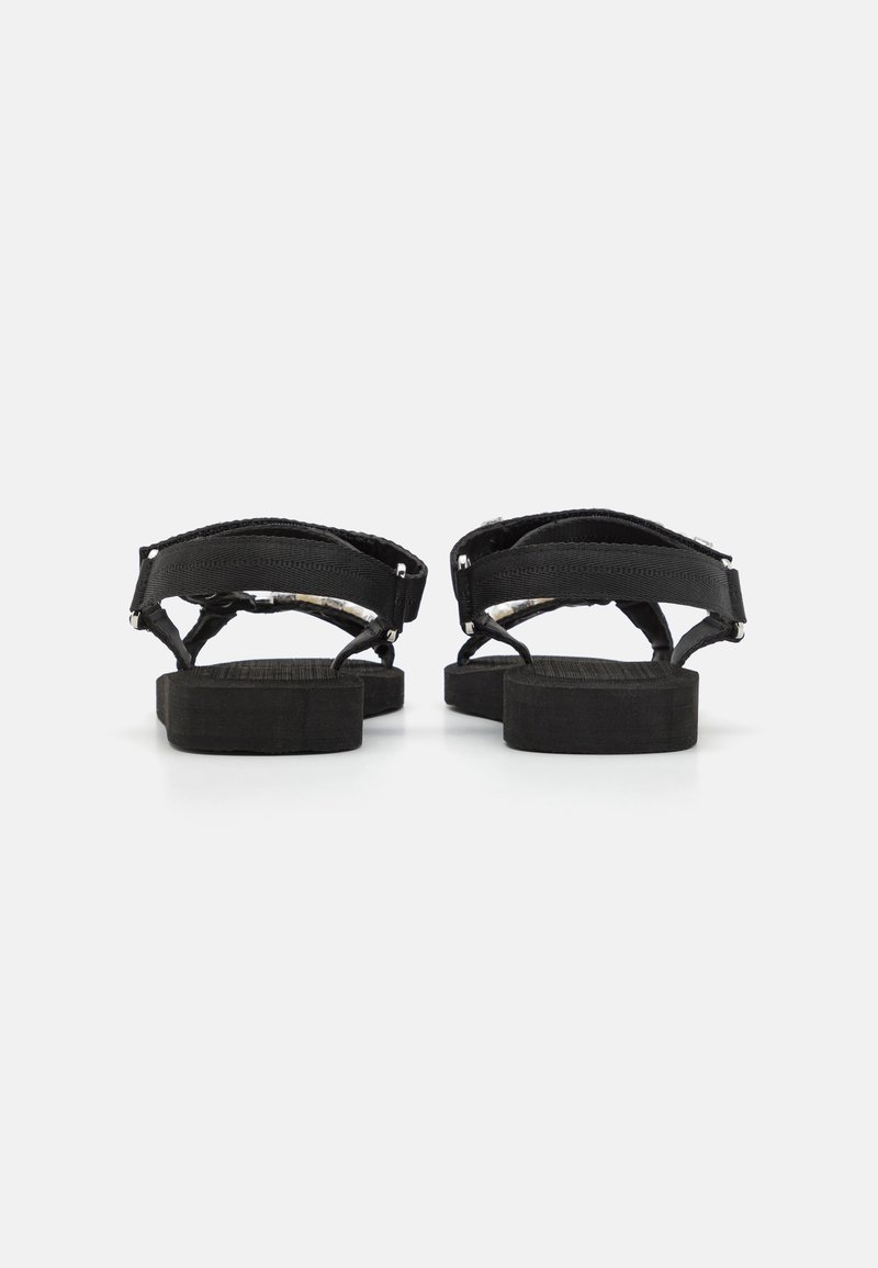 Sandales noires avec semelle texturée, présentant des sangles tissées et des boucles réglables. Design simple avec une construction plate et robuste.