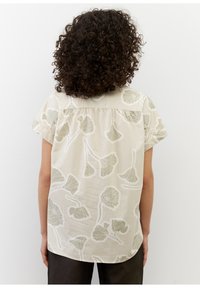 Korte mouwen blouse van lichtbeige stof met een botanische-print in gedempt groen. Loze pasvorm met een afgeronde zoom en detail op de rug.