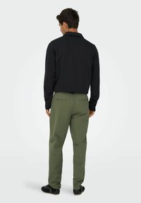 Schwarzer Pullover mit Kragen, kombiniert mit olivgrünen Hosen mit elastischem Bund und Seitentaschen, von hinten betrachtet.