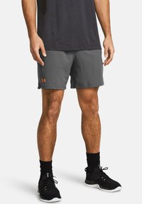 Pantalones cortos atléticos grises con cintura elástica y logo naranja en la pierna izquierda, combinados con zapatillas deportivas negras y calcetines.