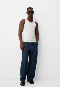 Vit ärmlös linne, löst sittande mörkblå jeans och svarta skor. Tillbehör inkluderar svarta solglasögon. Enkel bakgrund.