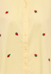 Chemise jaune à boutons sur le devant, ornée de fraises rouges brodées dispersées sur le tissu, fabriquée en matière légère et texturée.