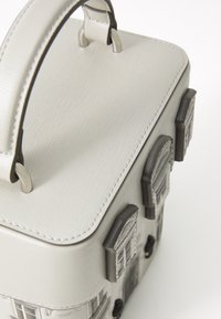 Petit sac à main gris clair conçu pour ressembler à une maison avec des fenêtres texturées et une poignée supérieure sur fond blanc.