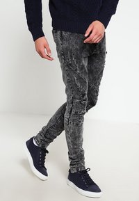 Czarne dżinsy z denimu z przetarciami i dopasowanym krojem, zestawione z granatowymi sneakersami o fakturowanej cholewce i białej podeszwie.