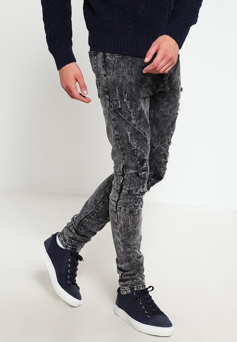 Czarne dżinsy z denimu z przetarciami i dopasowanym krojem, zestawione z granatowymi sneakersami o fakturowanej cholewce i białej podeszwie.