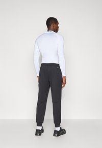 Λευκή αθλητική μπλούζα με μακριά μανίκια συνδυασμένη με μαύρο κολάν, που διαθέτει ελαστική μέση και στενές μανσέτες. Μαύρα αθλητικά παπούτσια ολοκληρώνουν την εμφάνιση.