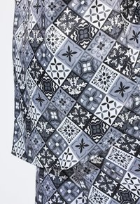 Černobílá tkanina s vzory obsahujícími různé složité květinové a geometrické designy v odstínech šedi, s hladkou, lesklou texturou.