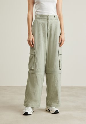 Φωτεινά πράσινα cargo παντελόνια με χαλαρή εφαρμογή, που διαθέτουν πλαϊνές τσέπες, κλείσιμο με κουμπί και υφασμάτινη υφή. Φοριούνται με λευκά αθλητικά παπούτσια.