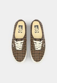 Brązowe trampki w wzór houndstooth z płócienka, z białymi sznurowadłami, gumową podeszwą i beżową wkładką z logo Vans na górze. Złote przeszycia jako akcenty.