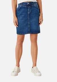 Falda vaquera en azul oscuro con botón en la cintura, cinco bolsillos y corte recto, combinada con zapatillas blancas. Textura lisa, estilo casual.