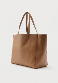 Καφέ τσάντα ώμου από δερματίνη με διπλούς ιμάντες, όρθια σε απλό λευκό φόντο.