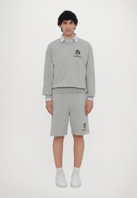 Set de hanorac gri și pantaloni scurți dintr-un material moale. Prezintă un logo pe piept și pe pantaloni. Include o cămașă cu guler dedesubt.