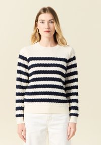 Maglione a righe nei colori blu navy e crema, con un motivo testiurato, polsini e scollatura a costine. Vestibilità aderente con tessuto leggero.