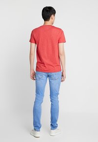 Camiseta roja de manga corta con cuello redondo, combinada con jeans ajustados de color azul claro y zapatillas blancas, vista desde la parte posterior.