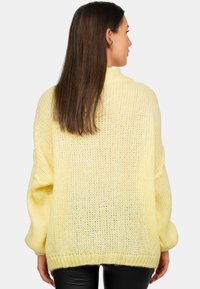 Pull en maille jaune surdimensionné avec un tissage lâche et texturé, et des coutures d'épaule basses. Présente un col haut et un ourlet côtelé.