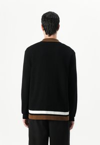 Svart stickad cardigan med brun krage och randig nederkant som har vita och mörkbruna ränder. Långa ärmar och ett strukturerat mönster.