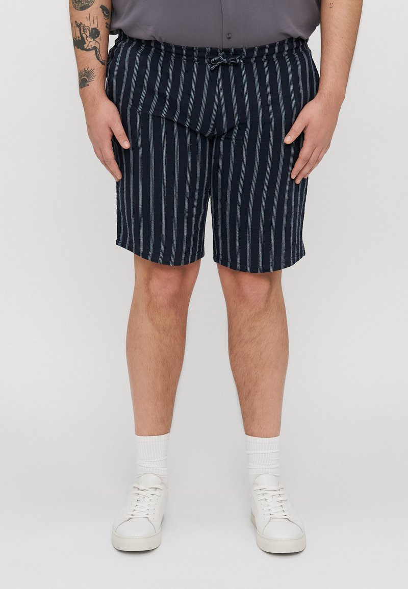 Marine-stripete shorts med elastisk midje og snor, laget av lett materiale. Kombinert med hvite joggesko og sokker i crew-lengde.