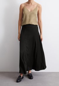 Débardeur en soie olive avec un décolleté en V, associé à une jupe maxi fluide en satin noir et des mocassins noirs. Texture lisse et design minimaliste.