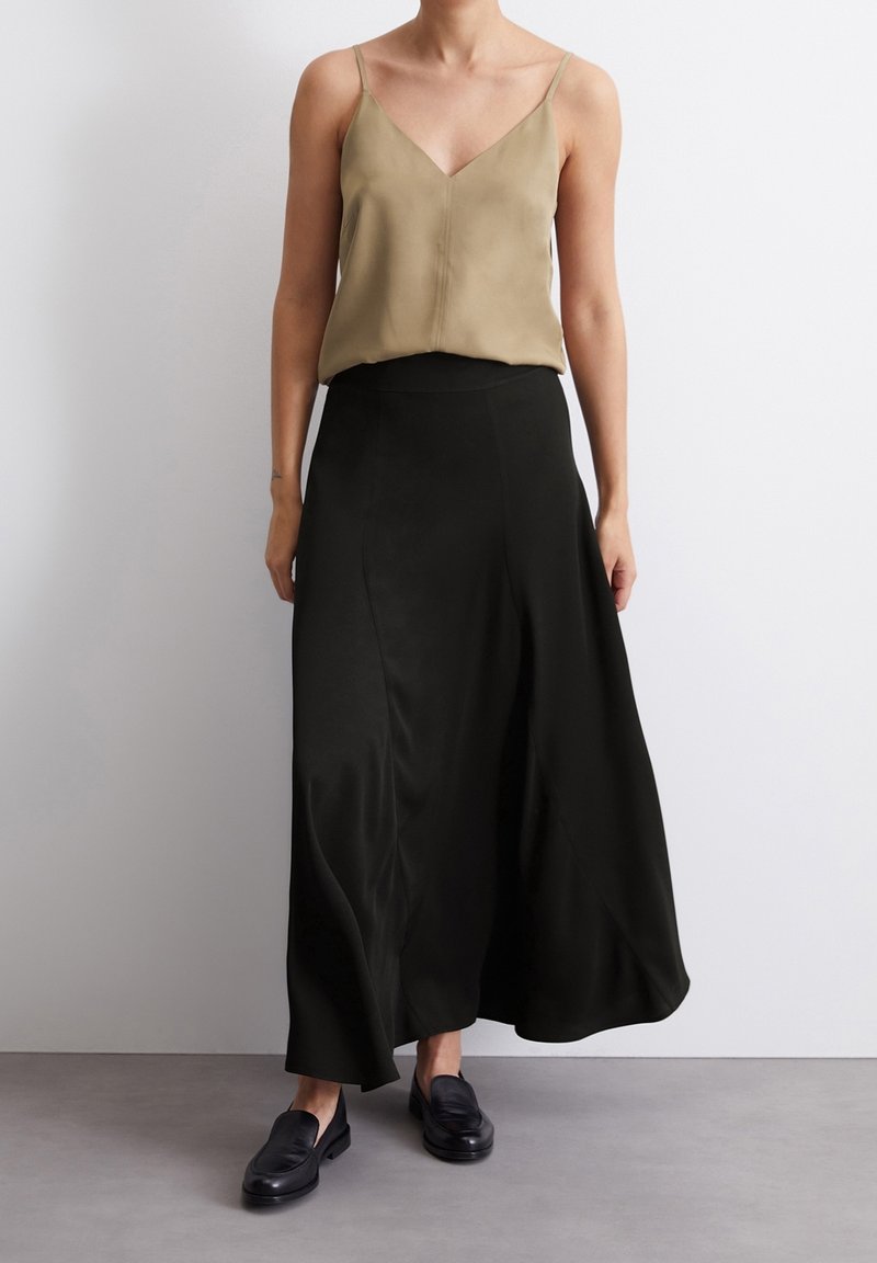 Débardeur en soie olive avec un décolleté en V, associé à une jupe maxi fluide en satin noir et des mocassins noirs. Texture lisse et design minimaliste.