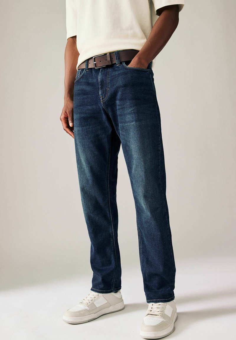 Dark blue denim jeans with a straight cut, featuring a brown leather belt and white sneakers. Smooth texture with subtle fading details.