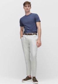 T-paita tummansinisellä lyhythihaisella mallilla, yhdistettynä vaaleanharmaisiin pellavahousuihin, ruskeaan punottuun vyöhön ja ruskeisiin kenkäpariin, joissa on valkoiset pohjat.