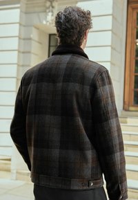 Brązowa flanelowa kurtka w kratę z ciemnym, miękkim kołnierzem. Wzór składa się z różnych odcieni brązu i szarości. Zapięcie na napy u dołu.