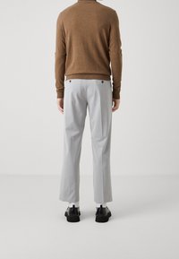 Maglione a maglia marrone, pantaloni beige chiaro su misura con taglio dritto e scarpe nere. I dettagli notevoli includono tasche posteriori e una consistenza morbida.