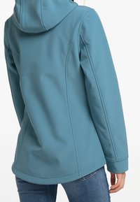 Veste softshell de couleur sarcelle avec une coupe ajustée, une capuche et des détails cousus. Texture lisse et taille légèrement cintrée.
