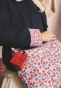 Borsa a tracolla con motivo floreale su sfondo blu, fiori rossi e una piccola pochette lucida rossa a pois attaccata al lato.