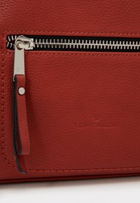 Röd strukturerad läderväska med silverfärgad dragkedja, svart foder, läderdragflik och präglad "TOM TAILOR"-logotyp på framsidan.