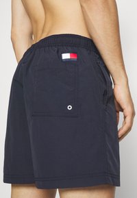 Mørkeblå svømmebukser laget av lett materiale, med elastisk liv, en baklomme med flaggpatch og detalj med hull.